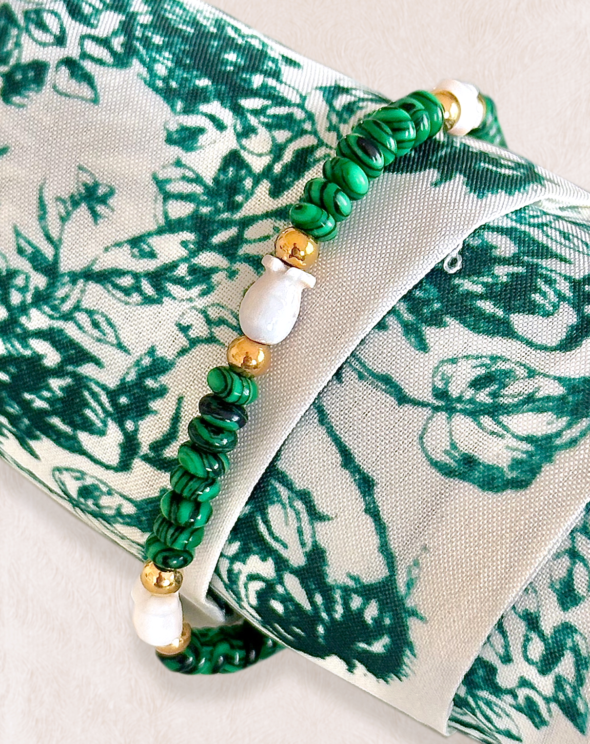 Bracelet de perles vertes, blanches et dorées enroulé autours d'un tissu à motif