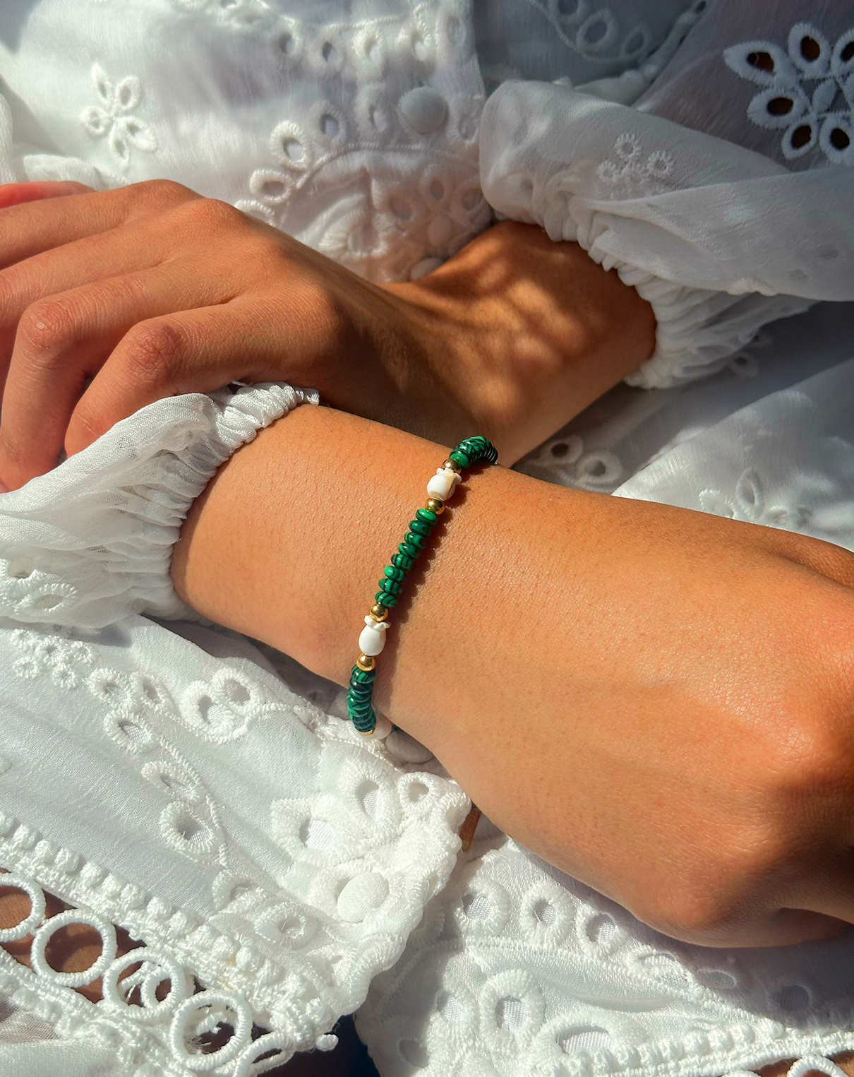 Bracelet de perles vertes, blanches et dorées autours d'un poignet