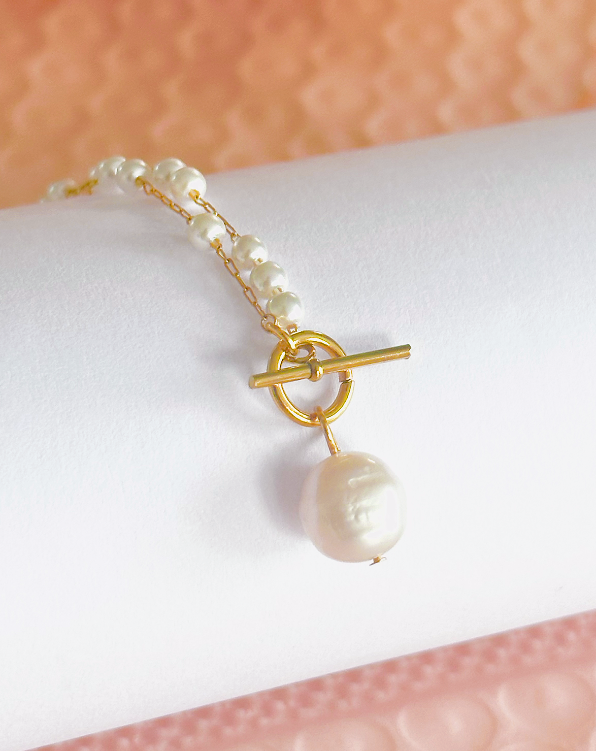 Collier, pendentif perle, attache au niveau de la perle par système de crochet sur cylindre blanc et fond rose 
